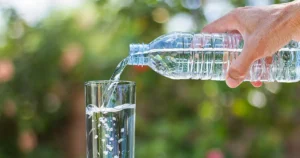 Glas Wasser wird mit Plastikflasche gefüllt